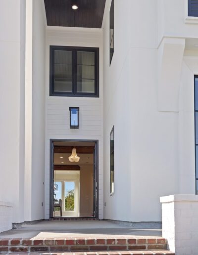 Modern house entrance with tall white walls, a dark wood ceiling, and a glass door flanked by windows.