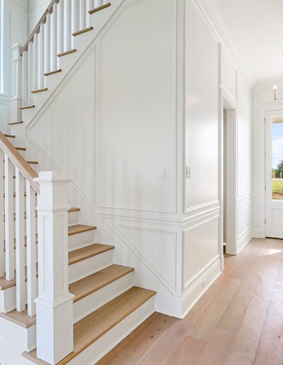 Bright entryway with wooden stairs and herringbone-patterned floor.