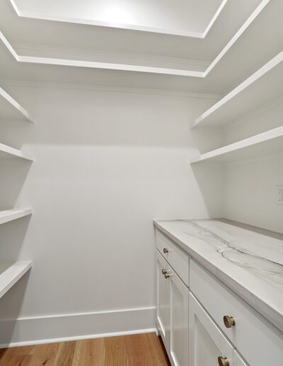 An empty, modern walk-in closet with white shelves, marble countertop, and wooden flooring.