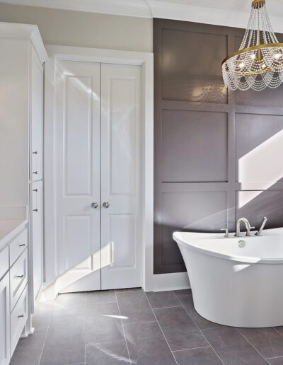 Modern bathroom with white fixtures, marble walls, and a chandelier.