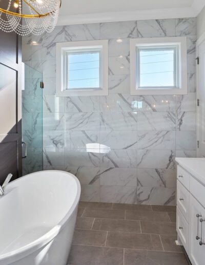 A modern bathroom featuring marble walls, a freestanding bathtub, a glass-enclosed shower, and a double sink vanity.