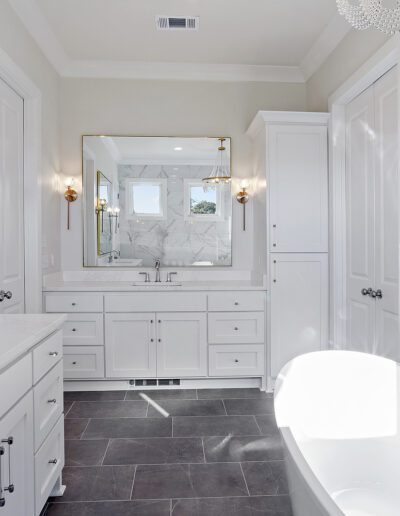 A modern bathroom featuring a double vanity, wall sconces, a large mirror, and a freestanding bathtub.