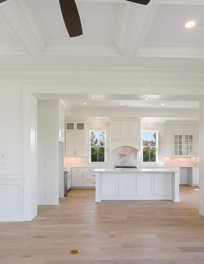 An empty, modern kitchen viewed from an adjoining room, featuring white cabinetry and marble countertops.