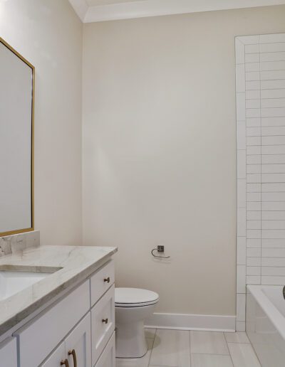 A modern bathroom with a white vanity, sink, mirror, and toilet, featuring subway tiles and neutral colors.