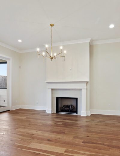 An empty living room with hardwood floors, a white fireplace, and a staircase to the right.