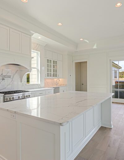 A bright, modern kitchen with white cabinetry, marble countertops, and hardwood floors.