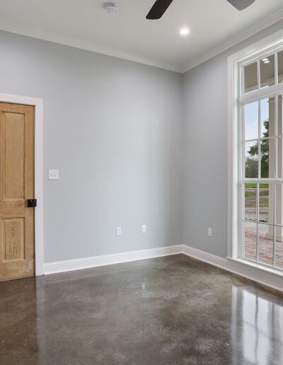 An empty room with gray walls, polished concrete floors, a wooden door, and a large window with white trim.