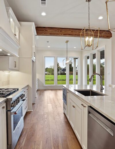 A modern kitchen with white cabinetry, stainless steel appliances, and a central island that opens up to a green outdoor view through sliding glass doors.