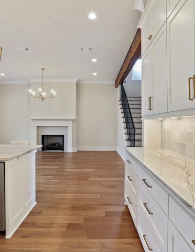 Modern kitchen with white cabinetry and marble countertops extending to a living area with a fireplace and staircase.