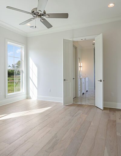 A spacious empty room with hardwood floors, large windows, and a ceiling fan.