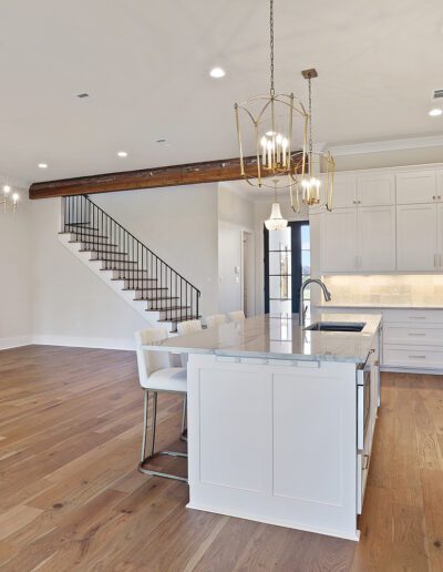 Modern kitchen with white cabinetry and stainless steel appliances adjacent to a living space with a fireplace and staircase.