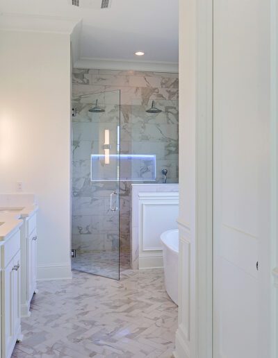 A bright, modern bathroom with marble finishes, a glass-enclosed shower, and a white vanity.