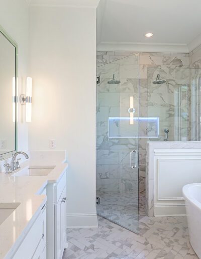 Bright and spacious bathroom with marble tiles, featuring a double vanity, glass-enclosed shower, and freestanding bathtub.