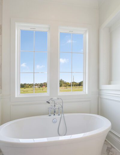 Bright bathroom with a white freestanding bathtub near windows overlooking a clear day.