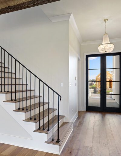 An empty foyer with wooden floors, a staircase with metal balusters and wooden handrail, and a glass-paneled door letting in natural light.