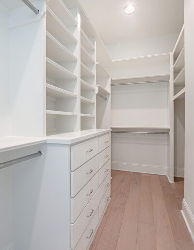 An empty, modern walk-in closet with white shelving and drawers.