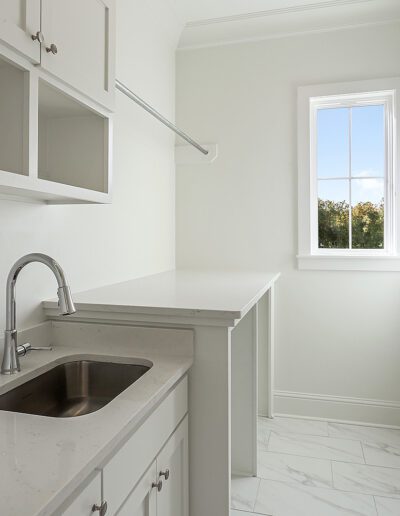 A clean and bright laundry room with white cabinetry, a stainless-steel sink, and a window with a view outside.