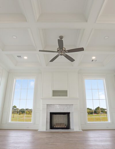 Spacious, well-lit living room with coffered ceilings, a ceiling fan, fireplace, and large windows.