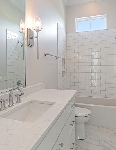 A bright, modern bathroom with white tiled walls, double sinks, and a glass-enclosed shower.