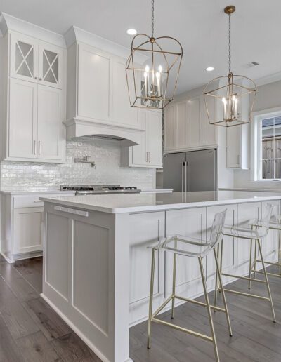 Modern kitchen interior with white cabinetry, marble countertops, and gold-accented bar stools.