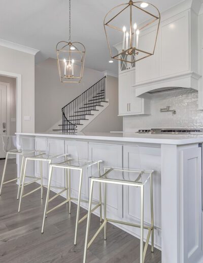 Modern kitchen interior with white cabinetry, a central island with bar stools, and elegant pendant lighting.