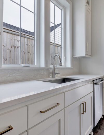 Bright kitchen with white cabinets, marble countertops, and a view of the yard through large windows.