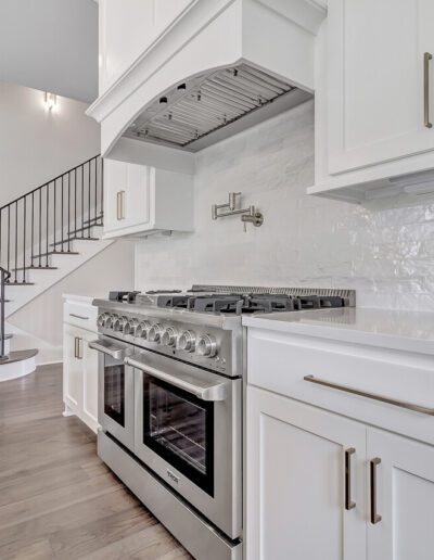 A modern kitchen with white cabinetry, stainless steel appliances, and a staircase in the background.