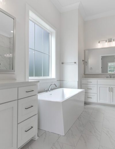 A bright, modern bathroom with white cabinetry, dual sinks, a freestanding tub, and marble accents.