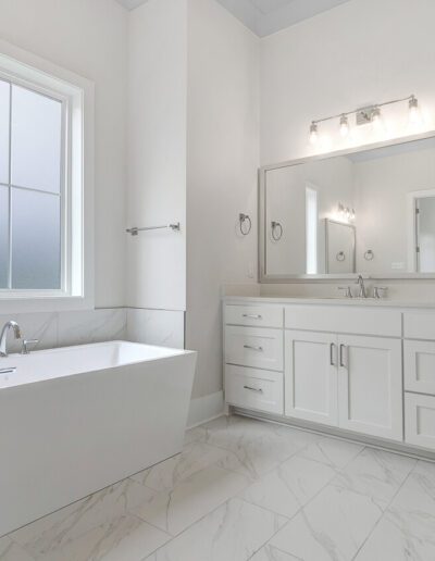 A modern bathroom with white cabinetry, a freestanding bathtub, and marble tiles.