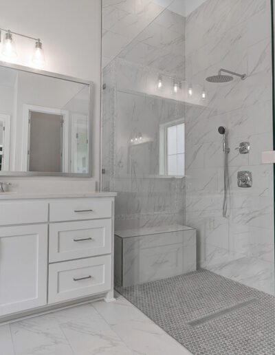 A modern bathroom with marble tiles, white cabinetry, and a glass-enclosed shower area.