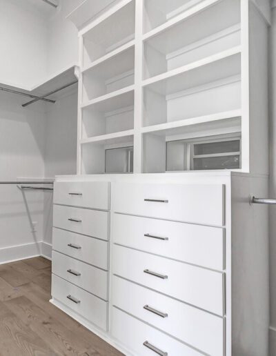 Empty walk-in closet with white built-in shelving and drawers.