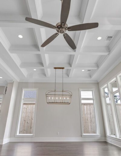 An empty modern living room with coffered ceilings, a ceiling fan, and large windows.