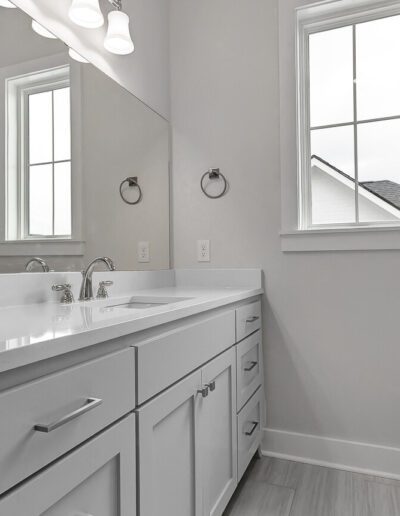 A bright, modern bathroom with white cabinetry and countertops, featuring a double sink and two mirrors under wall-mounted lights.