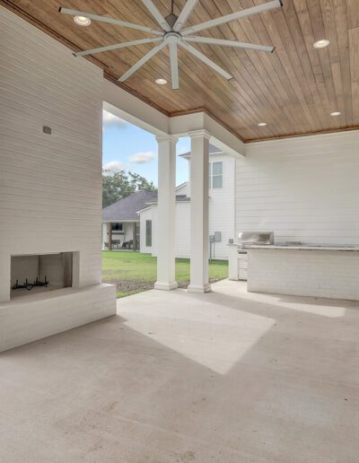 Spacious outdoor patio area with a fireplace and built-in grill, featuring a large ceiling fan and a view of the lawn.