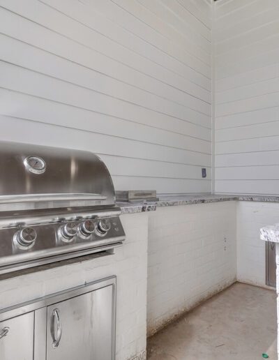 An outdoor kitchen corner featuring a stainless steel grill and marble countertops against white siding walls.