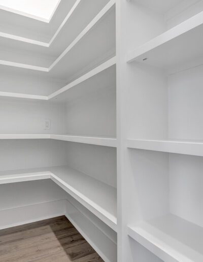 An empty walk-in closet with white shelves and wooden flooring.