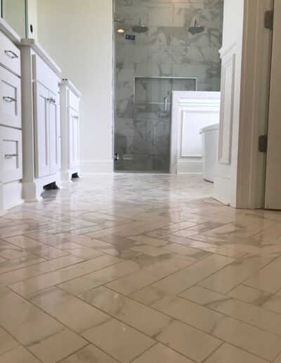 A clean and modern bathroom with white cabinetry and marble tile flooring.